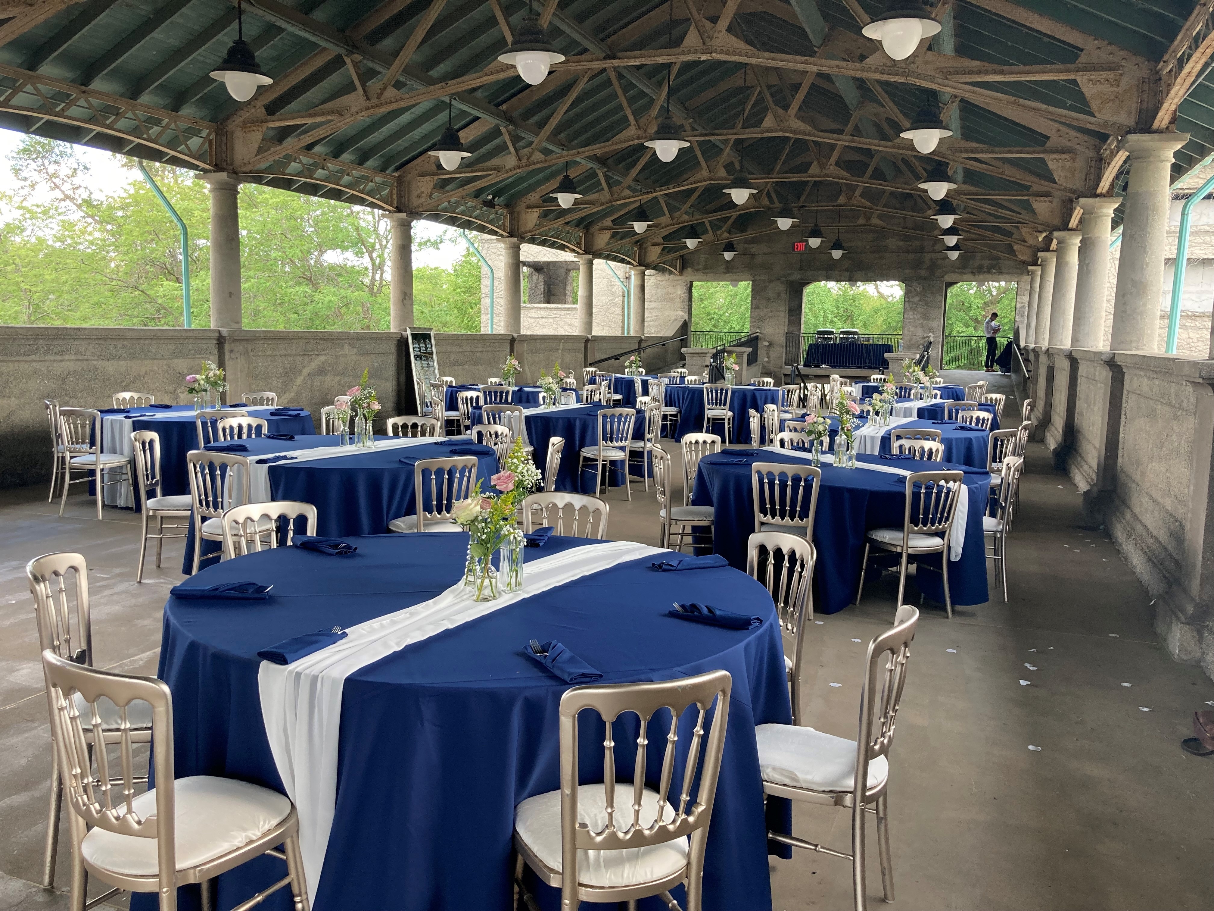 Outdoor wedding reception venue with round tables, navy blue tablecloths, and gold chairs.